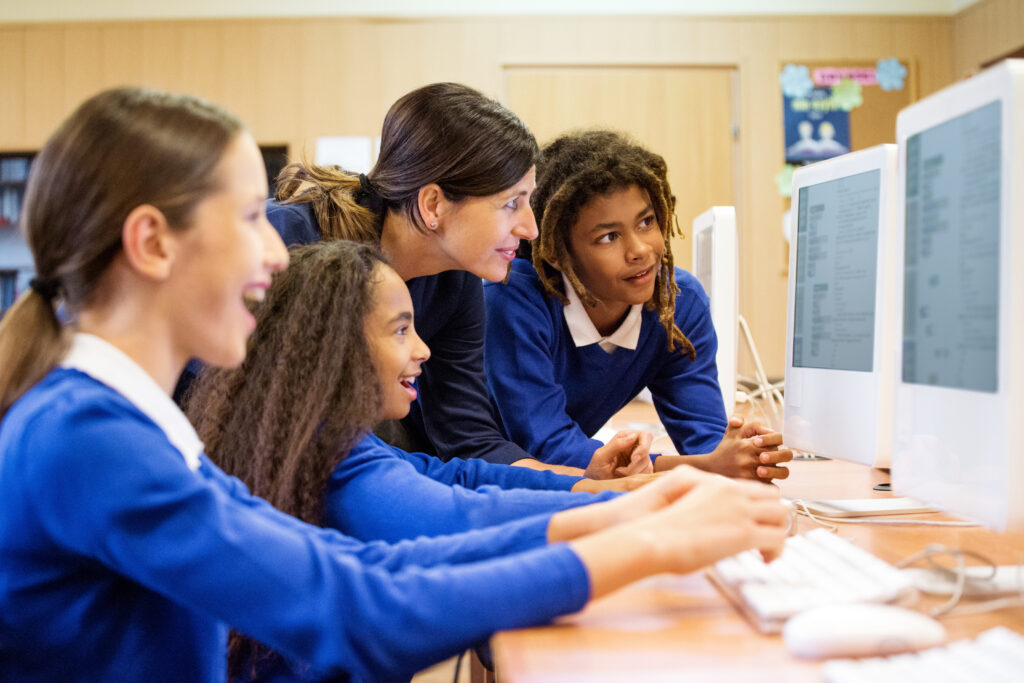 Online learning filler - Group of multi ethnic students coding in a computer lab. Teacher talking with them.